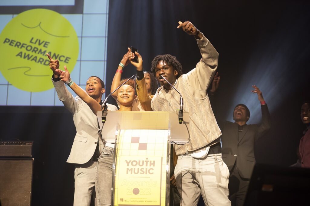 Three young black artists raiding their hands in celebration on stage.
